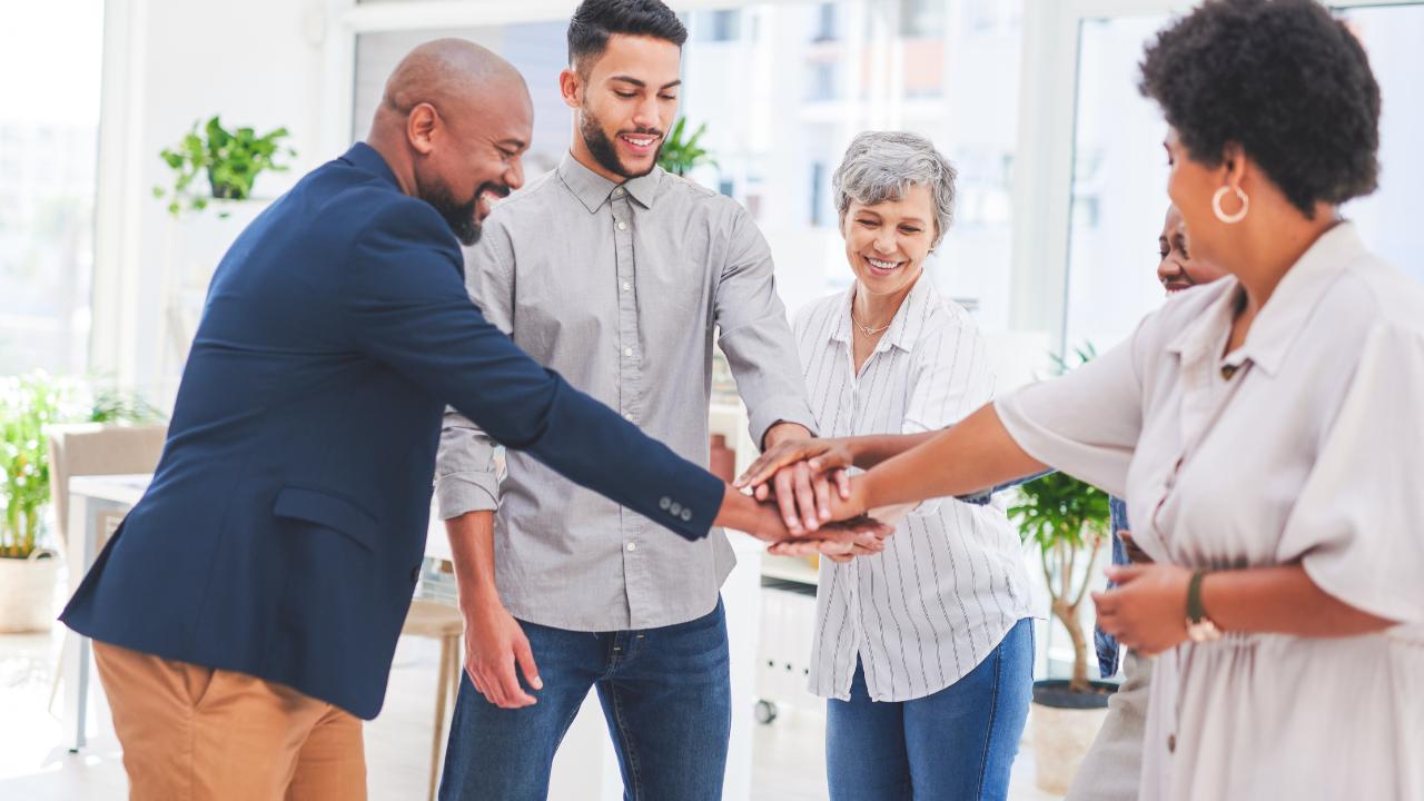 Grupo diverso de profissionais tocando as mãos juntos com entusiasmo, simbolizando como liderar uma equipe com alta performance.