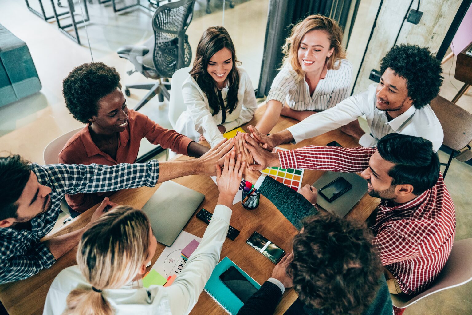 Equipe reunida ao redor de uma mesa juntando as mãos em gesto de união, representando como motivar sua equipe no dia a dia com ações simples.